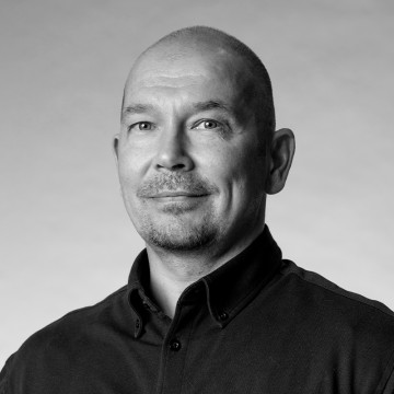 Mustavalkoinen muotokuva keski-ikäisestä miehestä, jolla on ajeltu pää, hento hymy ja leikattu pukinparta, yllään napitettu tumma paita, vaaleaa taustaa vasten.