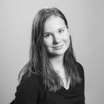 Nuori nainen, jolla on pitkät suorat hiukset ja tumma toppi, hymyilee lempeästi kameralle. Muotokuva on mustavalkoinen, ja taustalla on tavallinen tausta.