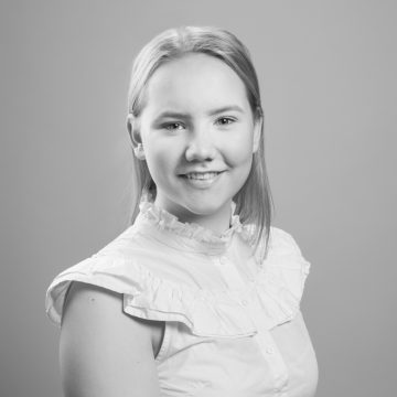 Nuori nainen, jolla on suorat, vaaleat hiukset, hymyilee kameralle. Hänellä on yllään röyhelöinen, hihaton, vaalea pusero. Kuva on mustavalkoinen, ja taustalla on tavallinen tausta.