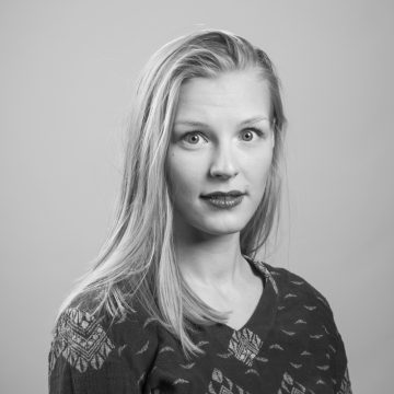 Mustavalkoinen muotokuva naisesta, jolla on pitkät, suorat hiukset ja joka katsoo suoraan kameraan yllättyneenä. Hänellä on päällään kuviollinen pusero ja hän on asettunut tavallista taustaa vasten.