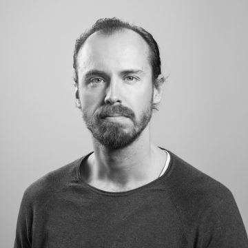 Mustavalkoinen muotokuva partaisesta ja viiksekkäästä miehestä, jolla on yllään tavallinen, tumma villapaita. Miehellä on lyhyet, liukuhiukset, ja hän katsoo suoraan kameraan neutraali ilme kasvoillaan.