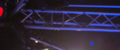 Kuvassa näkyy metallisia ristikkopalkkeja, joissa on lavavalaistus hämärässä ympäristössä, todennäköisesti osana konsertti- tai tapahtumakokonaisuutta.