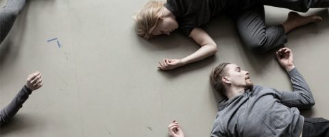Kolme ihmistä makaa vaalealla lattialla rennoissa asennoissa, kädet kevyesti taivutettuina ja silmät suljettuina tai keskittymättöminä, mikä viittaa rauhalliseen tai meditatiiviseen tilaan. Kuvaa katsotaan ylhäältä päin.