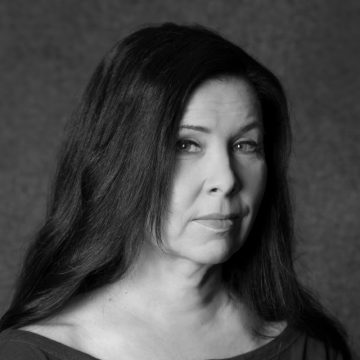 Mustavalkoinen muotokuva naisesta, jolla on pitkät tummat hiukset ja joka katsoo hieman kameran ohi neutraali ilme kasvoillaan, taustana tavallinen kuvio.