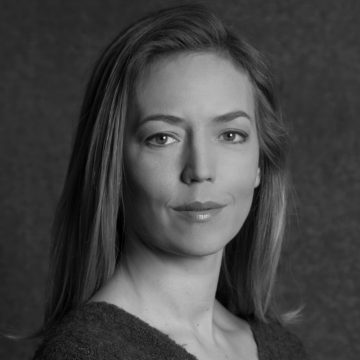 Mustavalkoinen muotokuva naisesta, jolla on suorat, olkapään pituiset hiukset, päällään kuvioitu toppi, ja joka katsoo rauhallisesti kameraan tummaa, yksinkertaista taustaa vasten.