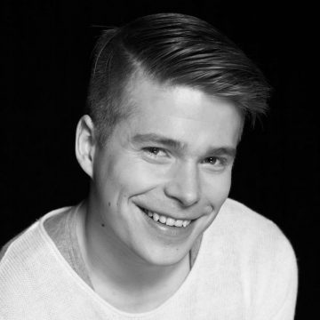Nuori mies, jolla on lyhyet, siististi laitetut hiukset, hymyilee lämpimästi kameralle. Hänellä on yllään vaalea villapaita ja hän on asettunut tummaa taustaa vasten. Kuva on mustavalkoinen.