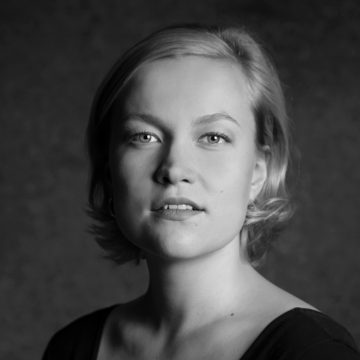 Mustavalkoinen muotokuva nuoresta naisesta, jolla on lyhyet vaaleat hiukset ja joka katsoo hieman ylöspäin. Hänellä on neutraali ilme ja päällään kaula-aukkoinen toppi. Tausta on pehmeästi sumea.