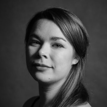 Mustavalkoinen muotokuva nuoresta naisesta, jolla on pitkät hiukset ja joka katsoo hieman sivulle. Valaistus korostaa hänen kasvonpiirteitään, ja hänellä on neutraali, rauhallinen ilme yksinkertaista taustaa vasten.