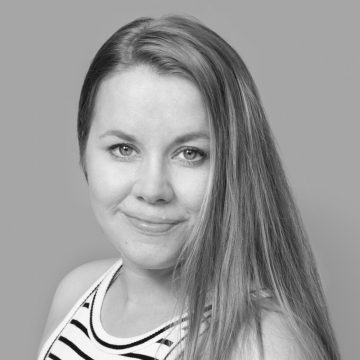 Nainen, jolla on pitkät, suorat hiukset ja hihaton raidallinen toppi, hymyilee pehmeästi kameralle harmaata taustaa vasten.