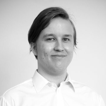 Vaaleaihoinen nuori henkilö, jolla on suorat, sivuille leikatut hiukset, hymyilee kevyesti, kun hänellä on valkoinen kauluspaita ja hän poseeraa vaaleaa taustaa vasten.