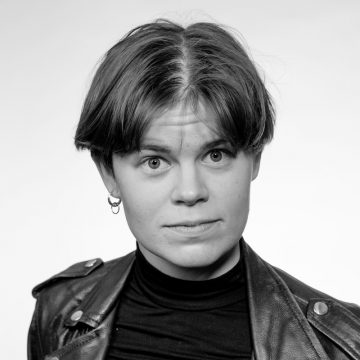 Mustavalkoinen muotokuva lyhythiuksisesta henkilöstä, jolla on musta poolokaulus ja nahkatakki ja joka katsoo suoraan kameraan neutraali ilme.
