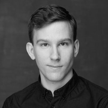 Mustavalkoinen muotokuva lyhythiuksisesta nuoresta miehestä, jolla on napillinen paita ja joka katsoo suoraan kameraan neutraalilla ilmeellä tavallista taustaa vasten.