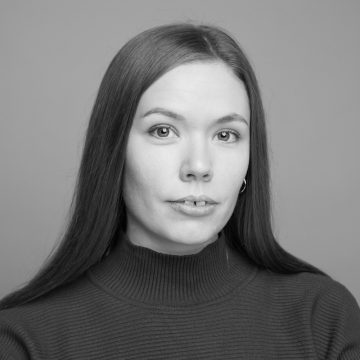 Mustavalkoinen muotokuva naisesta, jolla on suorat pitkät hiukset, päällään villapaita, joka katsoo suoraan kameraan neutraalilla ilmeellä tavallista taustaa vasten.