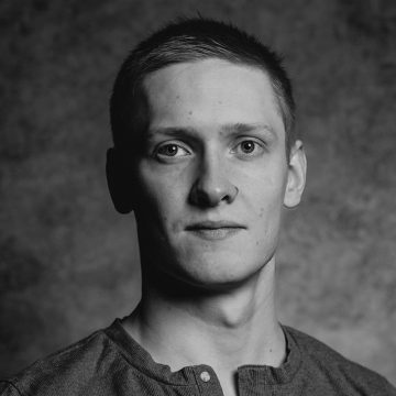 Mustavalkoinen muotokuva lyhythiuksisesta nuoresta miehestä, jolla on yllään rento napiton paita ja joka katsoo suoraan kameraan neutraalilla ilmeellä kuvioitua taustaa vasten.
