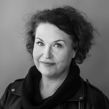 Mustavalkoisessa muotokuvassa kiharat hiukset ja vaaleat silmät omaava nainen hymyilee kevyesti, yllään tumma lehmänkauluksinen pusero ja nahkatakki.