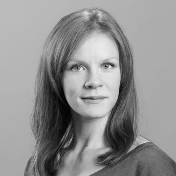 Nainen, jolla on suorat, olkapään pituiset hiukset, katsoo suoraan kameraan neutraali ilme kasvoillaan. Kuva on mustavalkoinen ja siinä on tavallinen tausta.