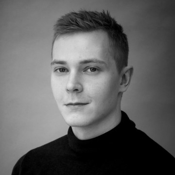 Mustavalkoinen muotokuva lyhythiuksisesta nuoresta miehestä, jolla on tumma poolopaita ja joka katsoo kameraan neutraalilla ilmeellä tavallista taustaa vasten.