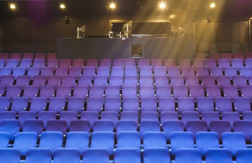 Tyhjä teatteri, jossa on violetteja ja sinisiä penkkirivejä, joiden edessä on ylävalojen valaisema ohjauskoppi takana.