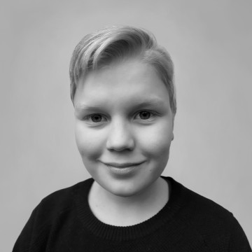 Mustavalkoinen muotokuva nuoresta henkilöstä, jolla on lyhyet vaaleat hiukset, tumma pusero yllään ja joka hymyilee hieman katsoessaan suoraan kameraan tavallista taustaa vasten.