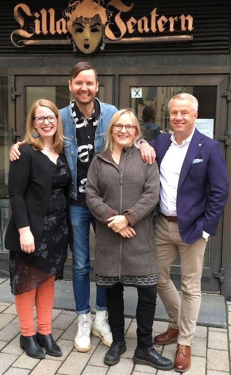 Neljä aikuista seisoo hymyillen teatterin sisäänkäynnin edessä, ja heidän yläpuolellaan on kyltti Lilla Teatern. Kolmella on silmälasit ja rennot vaatteet, yhdellä on sininen bleiseri. He poseeraavat tiiviisti yhdessä laatoitetulla jalkakäytävällä.