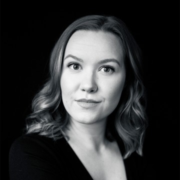 Mustavalkoinen muotokuva naisesta, jolla on aaltoileva tukka ja tumma toppi, joka katsoo suoraan kameraan neutraali ilme tummalla taustalla.