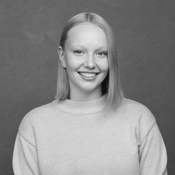Nuori nainen, jolla on suorat, hartioiden pituiset vaaleat hiukset, hymyilee kameralle. Hänellä on yllään vaalea villapaita, ja hän poseeraa yksinkertaista, kuvioitua taustaa vasten. Kuva on mustavalkoinen.