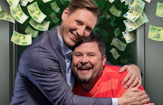 Kaksi hymyilevää miestä halaa toisiaan onnellisesti, toinen puvussa ja toinen rennossa raitapaidassa. Heidän ympärillään leijuu euroseteleitä vihreällä taustalla, mikä viittaa rahaan liittyvään iloon ja juhlaan.