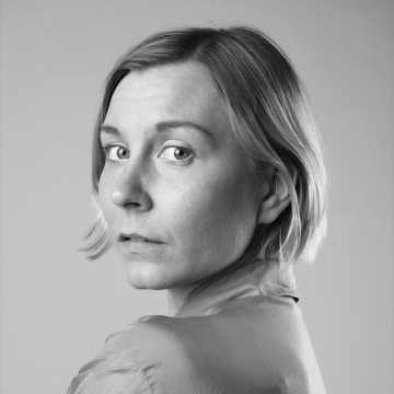 Mustavalkoinen muotokuva henkilöstä, jolla on lyhyet vaaleat hiukset, kauluspaita yllään ja joka katsoo olkapäänsä yli kameraan neutraali ilme kasvoillaan.