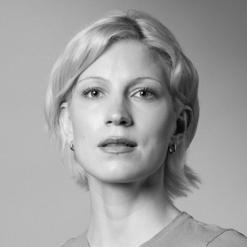 Mustavalkoinen muotokuva henkilöstä, jolla on lyhyet, vaaleat hiukset, yllään tavallinen toppi ja pienet korvarenkaat, katse hieman ylöspäin neutraali ilme. Tausta on tavallinen ja pehmeästi valaistu.